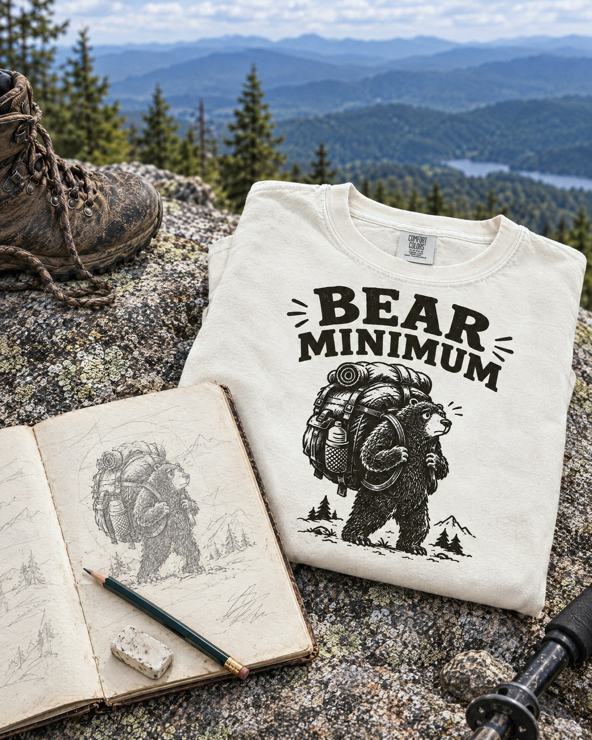 Trail sketchbook with the first pencil sketch of the Bear Minimum design beside the finished Blisterhood hiking t-shirt on a summit rock